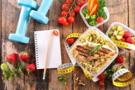 healthy food, hand weights measuring tape and note pad on a table