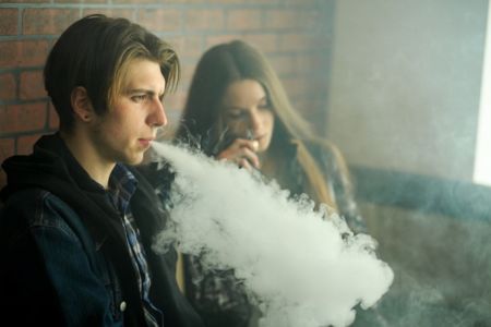 teenage boy and girl sitting outdoors and vaping